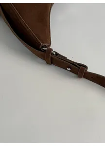 Detailed close-up of adjustable shoulder strap with metal buckle on dark brown suede bag