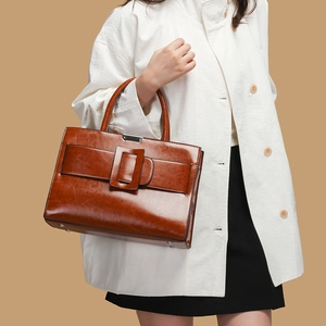 Brown glossy leather tote bag with large square buckle and top handle on model arm