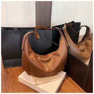 Détail d'un grand sac hobo marron montrant la texture du cuir et la large bandoulière