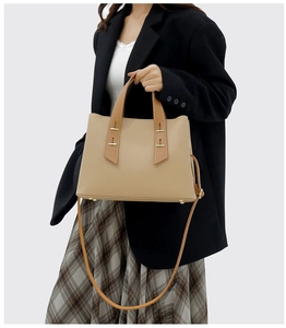 Detail of beige tote bag with litchi texture and gold hardware worn by professional model