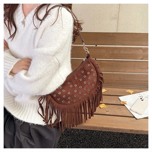 Brown suede crossbody bag with fringe tassels and eyelet details worn in outdoor setting
