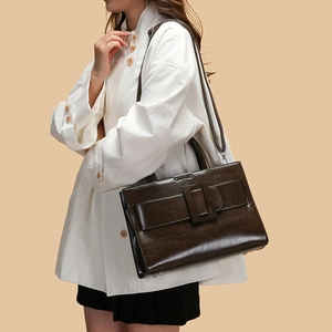 Detail of dark brown retro tote bag with square metal buckle on model with white jacket