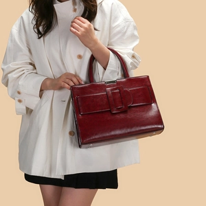 Detail of vintage burgundy leather tote bag with metallic buckle held by a model