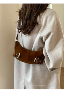 Brown suede crescent bag with silver buckles shown over a beige cashmere coat