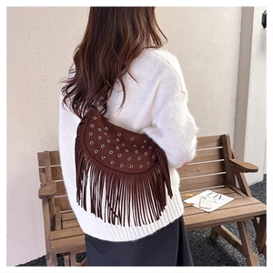 Detail of a brown suede half-moon bag with decorative metal rivets and long tassels