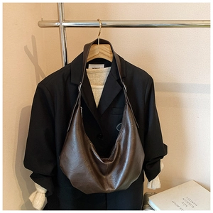 Détail d'un sac hobo en cuir marron brillant associé à un costume et une maille chic