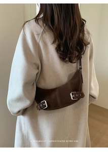 Close-up of brown suede moon bag with silver buckles worn over a beige coat