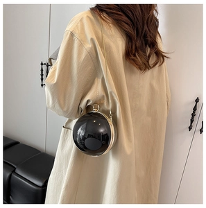 Détail d'un sac de soirée sphérique noir avec une chaîne dorée porté par un modèle