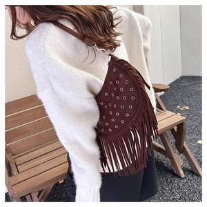 Close-up of brown suede crossbody bag with metal eyelets and long decorative tassels