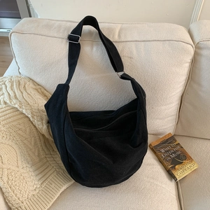 Minimalist black canvas hobo bag with adjustable wide strap on a soft beige background