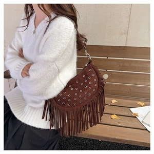 Close-up of brown suede crossbody bag featuring silver grommets and long tassel fringe details