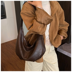 Détail d'un sac à bandoulière marron foncé brillant porté par un mannequin pour le quotidien