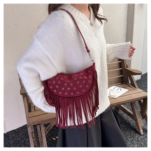 Detail of burgundy suede tassel crossbody bag with metallic eyelets and long fringe