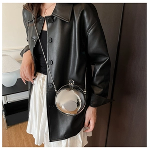 Détail du sac sphère en acrylique argenté avec chaîne sur un manteau en cuir noir