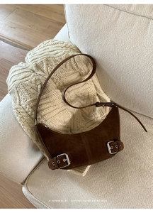 Close-up of brown suede crescent bag with silver buckles on a beige knit sweater background