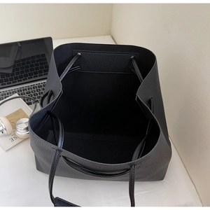 Top-down view of black lychee grain leather drawstring tote bag with office accessories