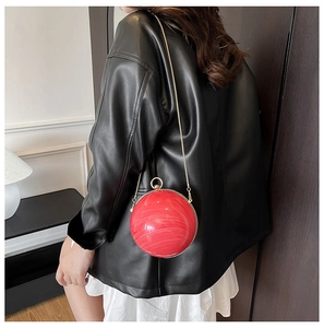 Détail du sac boule en acrylique rouge marbré avec chaîne dorée porté par un modèle