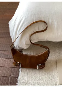 Close-up of brown suede crescent bag with silver buckles on beige plush rug