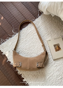 Close-up of brown suede hobo bag with silver buckles on white fringed carpet