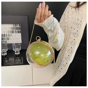 Détail du sac boule en acrylique à texture marbre vert et chaîne dorée tenue par un mannequin