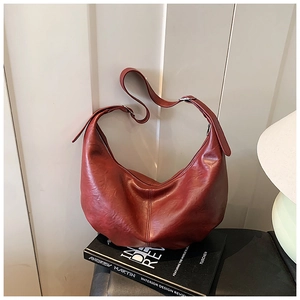 Détail du sac hobo en cuir bordeaux à texture plissée sur des livres décoratifs