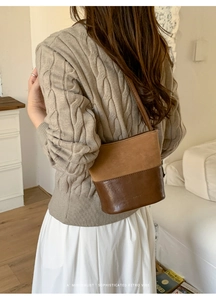 Détail d'un sac seau vintage bicolore porté à l'épaule avec logo embossé sur le bas