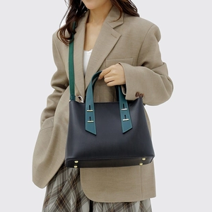 Minimalist black pebbled tote bag with green handles and crossbody strap on a model
