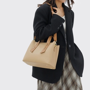 Beige tote bag with brown handles and gold hardware shown on model in black blazer