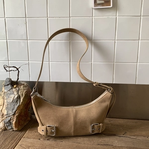 Retro camel suede crescent shoulder bag with vintage silver buckle details on wood base