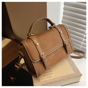 Gros plan du sac bandoulière marron mat avec boucles dorées et texture en daim vintage