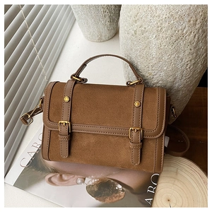 Gros plan d'un sac cartable en daim marron avec boucles dorées sur socle en bois