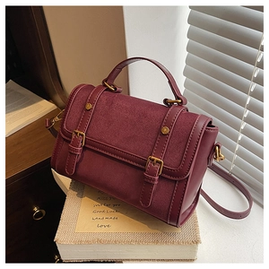 Détail du sac messager en cuir bordeaux avec texture suédée et boucles dorées