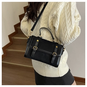 Détail du sac à main en cuir mat noir avec boucle dorée et poignée porté par un mannequin