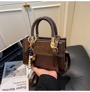 Detail of dark brown leather Boston bag with woven handle and colorful beaded charm