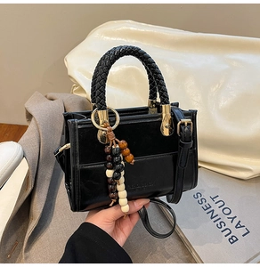 Close-up of black PU leather bag featuring woven handle and wooden bead charm detail