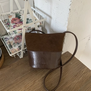 Retro deep brown bucket bag in matte suede and smooth leather on a wooden desk