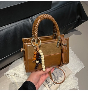 Detail of a brown textured crossbody bag with woven handle and beaded charm accessory