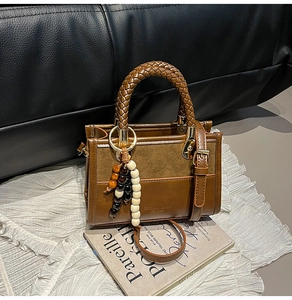 Detail of a brown bag with woven handle and colorful wooden beads on white fabric