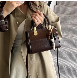 Detail of brown leather handbag with woven handle and colorful beaded charm on a trench coat