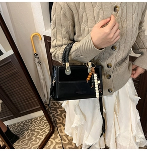 Detail of black leather crossbody bag with woven handle and beaded tassel pendant