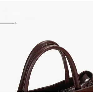 Detailed close-up of dark brown leather tote bag handles with precise stitching and metal zipper