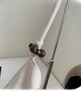 Detail of off-white shoulder bag strap featuring a large knot and polished wooden beads