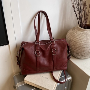 Large burgundy leather travel tote bag on a suitcase with premium matte finish and silver rings