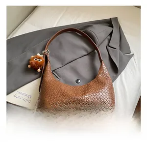 Detail of woven leather texture on a brown hobo shoulder bag with a plush charm
