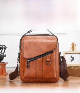 Vintage brown leather crossbody bag detail with diagonal zipper and metal D-ring on wood