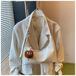 Close-up of beige woven texture hobo bag with a cute brown bear charm on white blazer