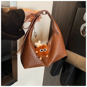 Detail of a dark brown woven hobo bag with checkered texture and a plush monster charm