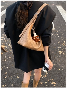 Khaki woven hobo shoulder bag with brown plush monster charm shown in street view style