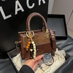 Deep brown leather handbag with woven handle and beaded charm in a luxury gift box