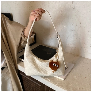 Detail of woven beige shoulder bag featuring a cute plush bear charm in a lifestyle setting